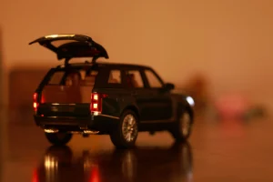 Vista trasera de un Land Rover a escala 1:64 en color verde oscuro con el maletero abierto y las luces traseras encendidas, reflejándose sobre una superficie de madera bajo una luz cálida.