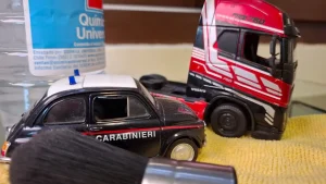 Un coche de policía Carabinieri en miniatura y la cabina de un camión Volvo rojo al lado de una brocha de limpieza suave y una botella de solución química.