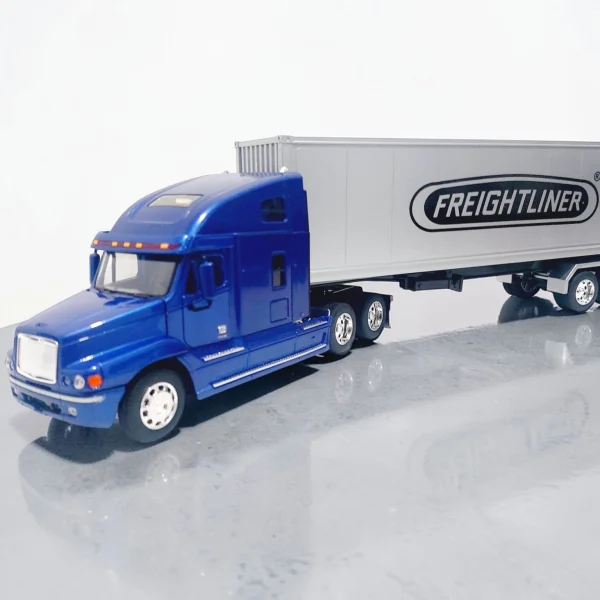 Vista frontal lateral izquierda del conjunto Freightliner Century Class 6x4 azul con semiremolque furgonado blanco escala 1:32 de Welly, mostrando cabina, ejes y emblema.